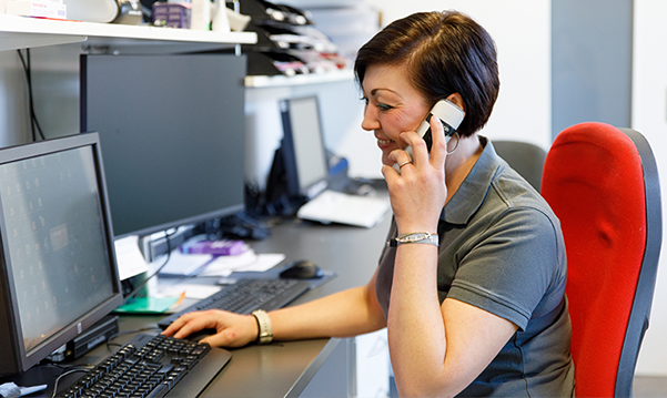 Eine Apothekerin der Petrisberg Apotheke sitzt im Büro und arbeitet mit dem PC, gleichzeitig führt sie ein Telefonat.