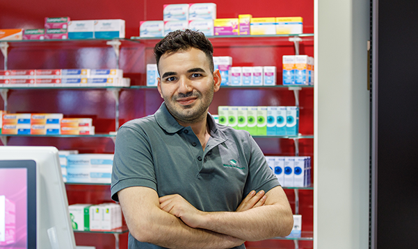 Der Inhaber der Petrisberg Apotheke steht vor dem Medikamentenregal und blickt in die Kamera.