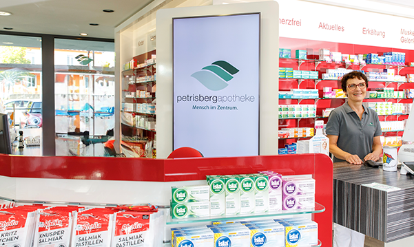 Eine Apothekerin der Petriesberg Apotheke steht hinter dem Tresen, im Hintergrund stehen ein Medikamentenregale.